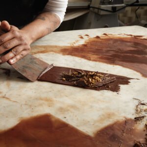 Black man chief collects cooled melted chocolate from marble tab