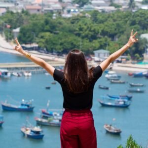rear-view-woman-with-arms-raised-standing-against-ships-harbor